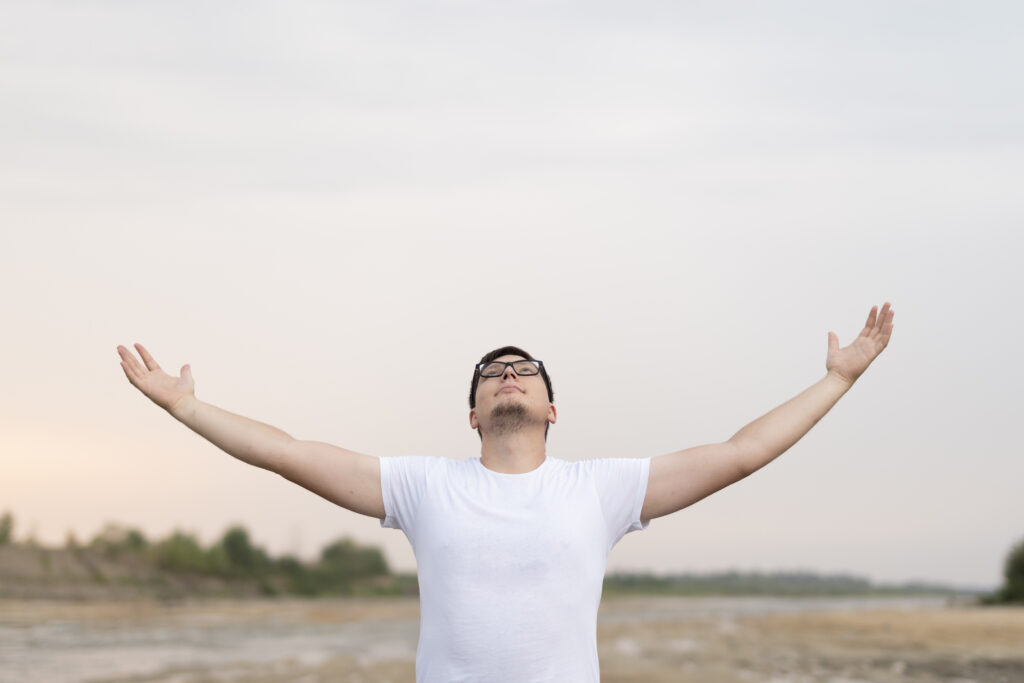 A man on a shoreline with arms outstretched to the sky, symbolizing mental resilience.